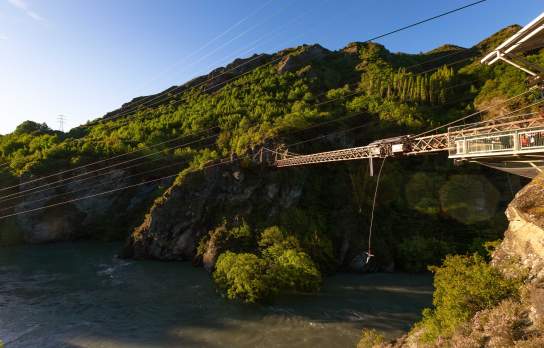 Wide shot of someone bungy jumping off a bridge over a river