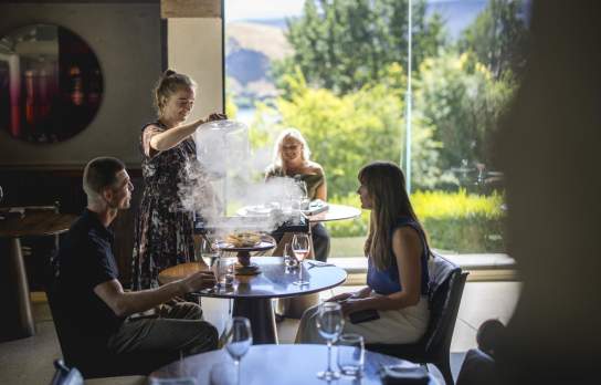 Waitress serving guests at Amisfield Restaurant, lifting up a lid of a dish with smoke coming up
