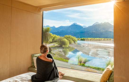 Woman looking out a huge window with view of mountains and lake at Kinloch Wilderness Retreat