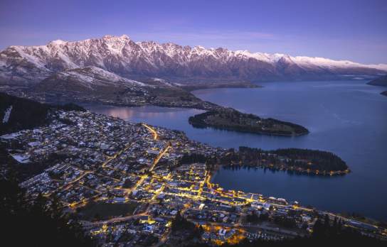 Aerial shot of Queenstown on a winters evening with town street lights glowing and snow capped mountains in the background