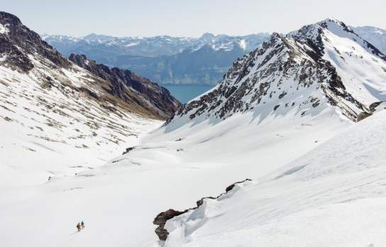 Two small figures in the distance with a wide view of Mount Larkins showing snowy mountain peaks and Lake Whakatipu