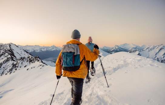 Point of view image with two people snow shoeing surrounded by snow covered mountains