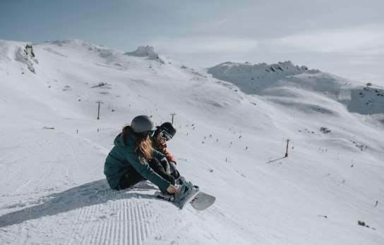 Couple strapping on snowboards at Cardrona Alpine Resort