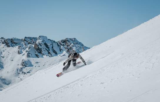 Spring snowboarder shredding a slope at The Remarkables with blue sky and mountains in the background
