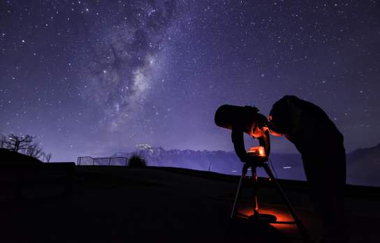 Person with telescope stargazing underneath the milky way near The Remarkables mountain range