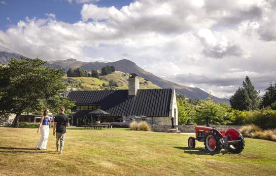 Two people walking along a lawn towards a restaurant with views of mountains in the background