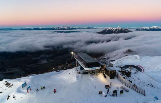 Soft warm hues of the sunrise at Coronet Peak with mountain poking out above clouds