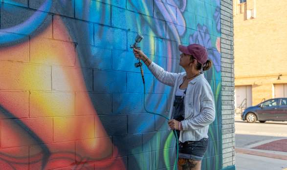 Artist Mindy Allen painting her mural titled Stop and smell the flowers as part of the BOOM! Salina mural festival