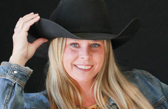 Stephanie Andrews in western attire - woman with long blond hair and blue eyes in black cowboy hat wearing denim jacket and southwestern printed blouse