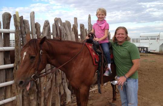 little girl riding horse with her dad standing next to her