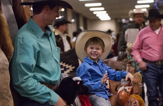 young boy smiling wearing a cowboy hat in a crowd of people