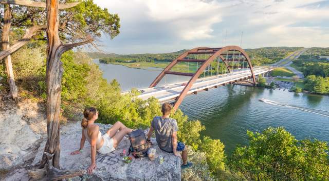 Hikers sitting on a hilltop rock overlooking the Pennybacker Bridge at Lake Austin.