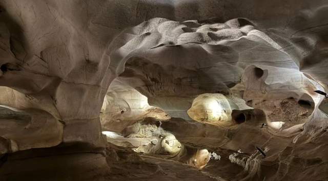 A winding walking path through Longhorn Cavern with sleek, beige rock walls on either side and large arched ceilings.