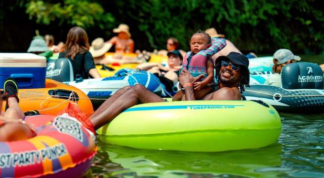 A man sitting in a neon green inner tube floating on a river surrounded by other people in tubes.