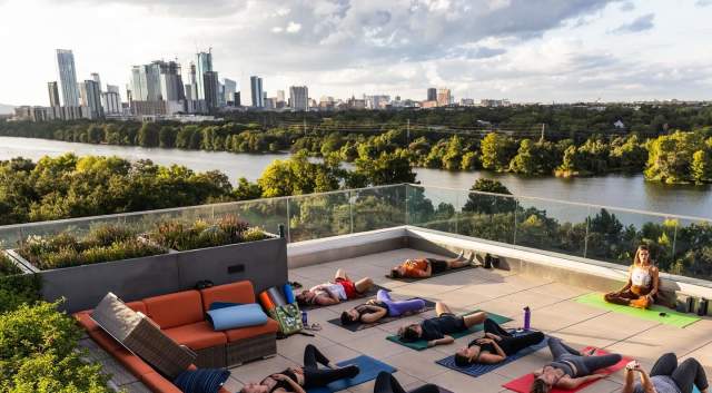 People doing yoga on a rooftop building with the Austin Skyline in the background.