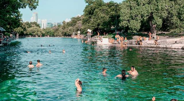 Adults and children playing in and along the banks of Barton Springs Pool.