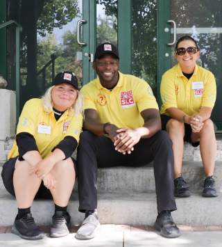 Three people sitting on steps wearing yellow downtown ambassadors shirts