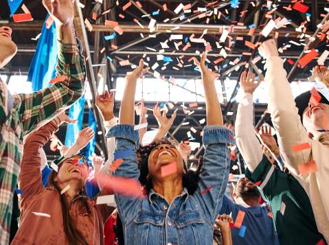 People with their arms up, cheering and confetti falls on them
