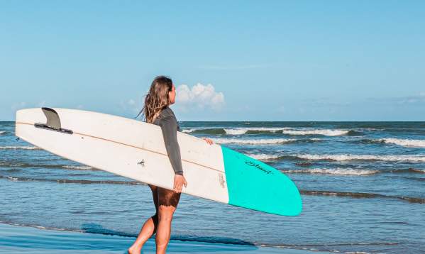 Girl holding a white and blue surf board walking into the water.