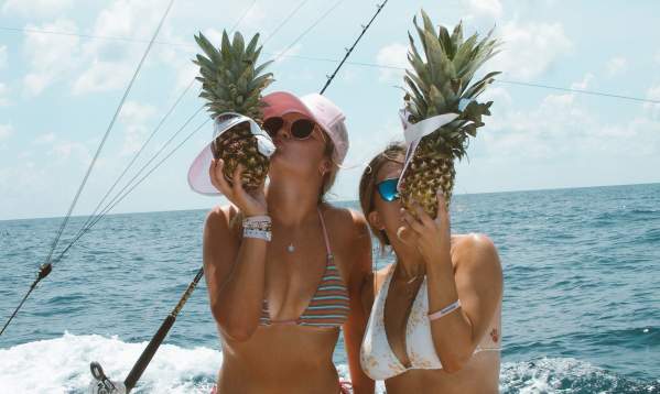 Two girls on a boat kissing pineapples