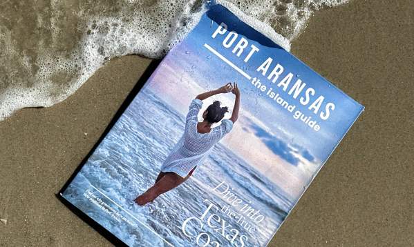 The island guide book in the sand with a wave going over top.