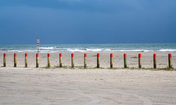 Bollards with a red top in the middle ground with blue water behind and sand in front