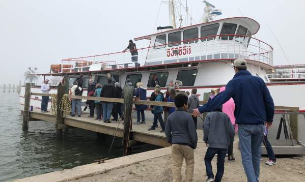 A group of kids and adults waits in line to board a large white boat