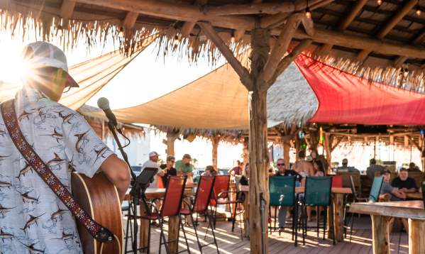 Photo from behind a musician playing guitar towards a tiki bar