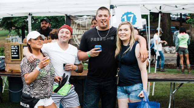 A lively group of friends shares drinks and laughs at a local Fayetteville festival, exuding fun, freedom, and community spirit under a row of white vendor tents.