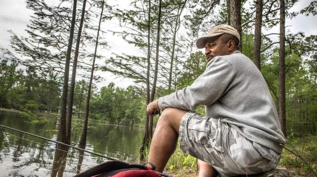 Man fishing along the shoreline at Carvers Creek State Park, surrounded by pine trees and calm water.