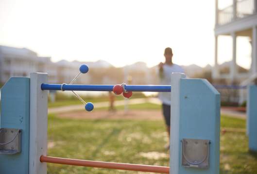 A blue ladder ball wraps around the top wrung next to a red already wrapped around. The man who threw the ladder ball is out of focus in the back