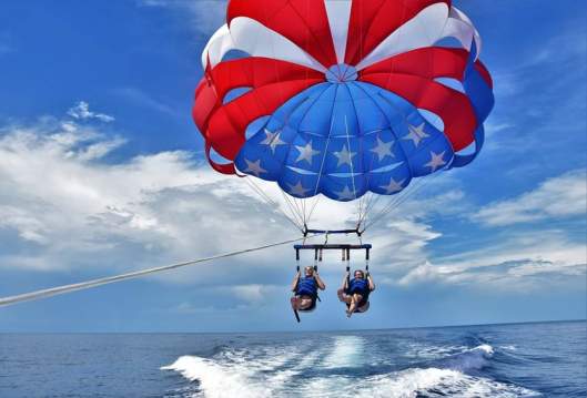 Two people being pulled above the water by a star-spangled parasail