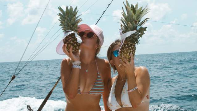 Two girls on a boat kissing pineapples