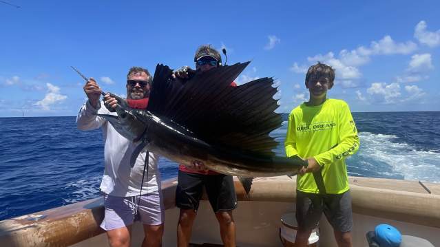 A fisherman holds a large sailfish out of the water next to a boat in Port Aransas.