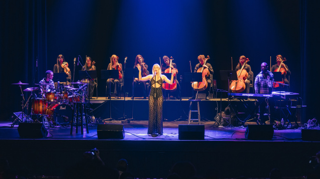 Grace Weber singing at a stand up mic with a string octet behind her
