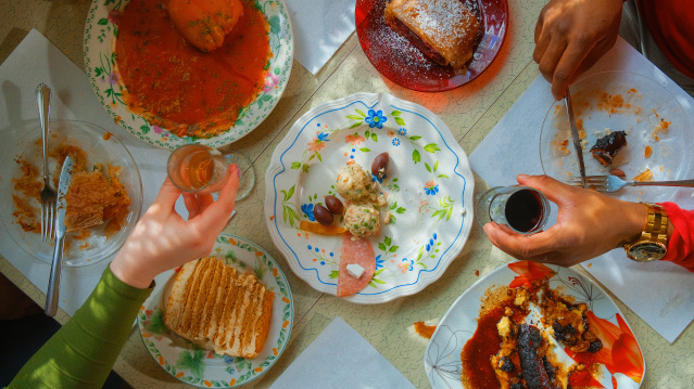 two hands holding small wine glasses over a table of half-eaten appetizers