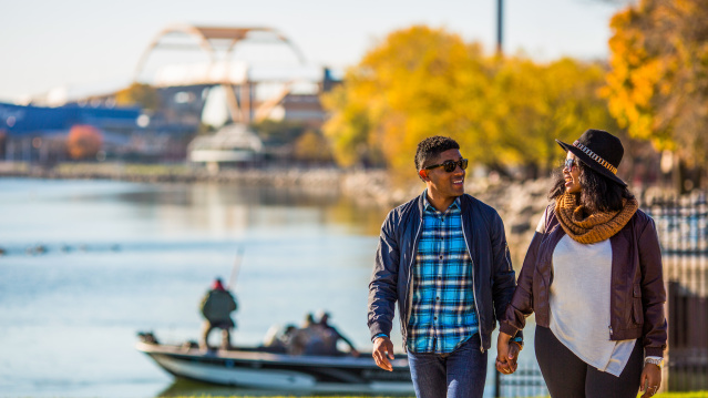 a couple walking and holding hands with fall foliage in the background