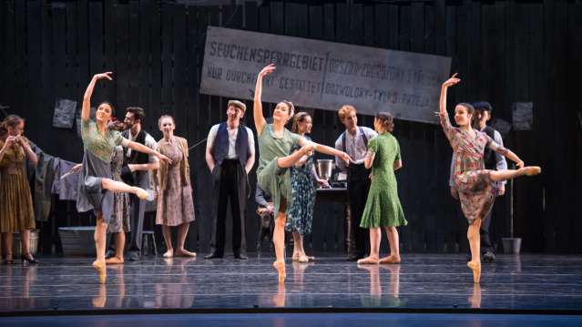 A group of ballet dancers perform onstage in vintage-style dresses, striking elegant poses with lifted arms and extended legs, while other performers in period clothing watch from behind.