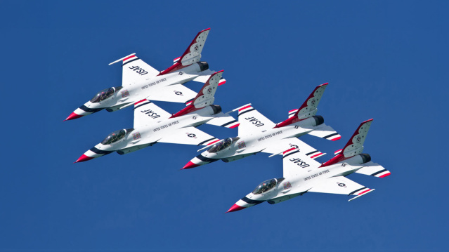 Four jets performing air & water show maneuvers against a cobalt blue sky