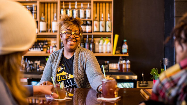 A bartender serving a non-alcoholic cocktail to two bar patrons.