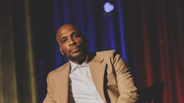 Ali Siddiq on stage leaning on a stool.