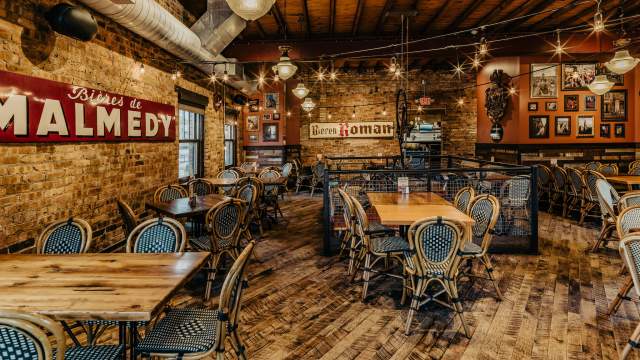 A warm, rustic restaurant interior with exposed brick walls, wooden beams, vintage signage, and neatly arranged tables and chairs.