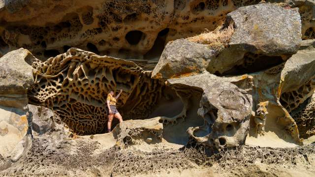An individual stands against a wall of unique sandstone formations.