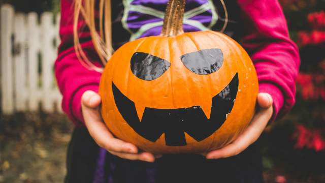 Close-up of a cheerful jack-o'-lantern pumpkin held by a child’s hands, celebrating Halloween.