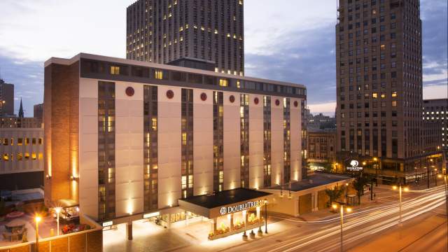 The DoubleTree by Hilton Hotel illuminated by lights against a dimly lit sky, with buildings in the background.