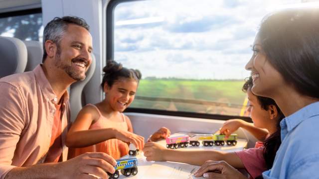 Family riding on Brightline train while kids play with toy train