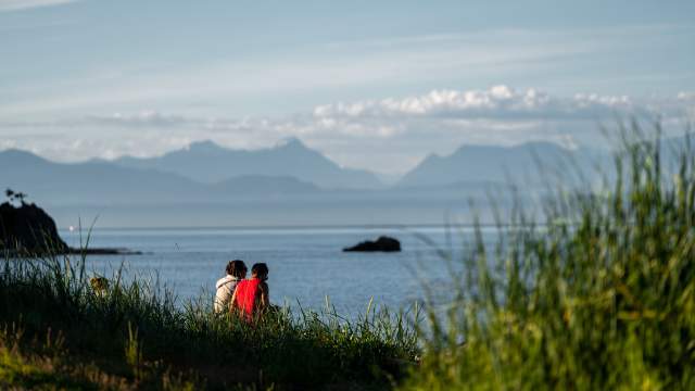 Two people seated on the grass watching the ocean.