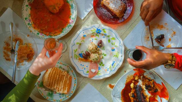 two hands holding small wine glasses over a table of half-eaten appetizers