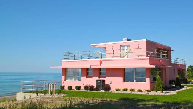 Beautiful pink house atop a dune in front of a lake.