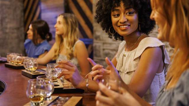 Women at a bar tasting bourbon and talking.